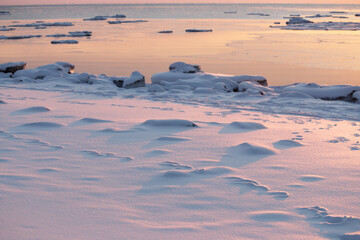 Snow on winter beach and calm sea at sunrise