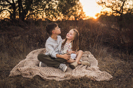 Young girl and boy sitting on blanket in California field at sunset