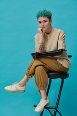Portrait of teenage girl with prosthetic arm posing on chair against blue background