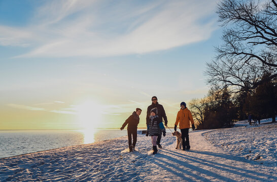 Father and sons walking a dog along a snowy path at sunset