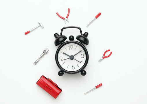 A flatlay picture of alarm clock with tools miniature on white background. Repairing time and fixing