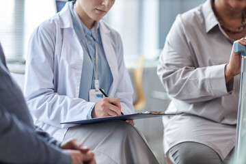 Close up of female therapist writing on clipboard while overseeing mental health support group for seniors, copy space