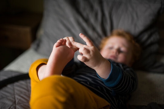 Young boy picking at his toenails while laying on bed at home