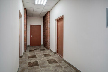 white empty long corridor with red brick walls and doors in interior of modern apartments or office