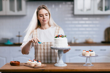 Pastry chef confectioner young caucasian woman prepare cream cake on kitchen table. Cakes cupcakes and sweet dessert