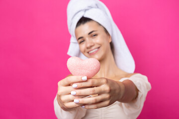 Beautiful cheerful attractive girl with a towel on her head, holds a sponge in the form of a pink heart.