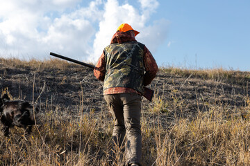 Mature man hunter with gun while walking on field.