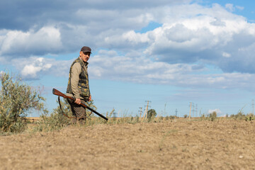 Mature man hunter with gun while walking on field.