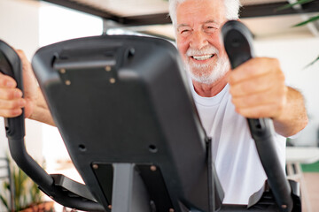 People sport concept. Portrait of happy senior man cycling doing exercises to stay fit. Elderly bearded man riding stationary bicycle in home terrace