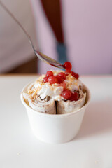 A worker is decorating a rolled ice cream tub with strawberry bubble toppings with a spoon