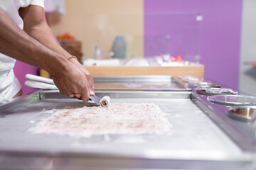 Obraz premium A worker is using a spatula to roll an ice cream on a freeze machine