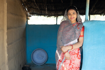 Young rural indian woman wearing sari standing at village home.