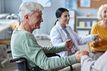 Fototapeta premium Side view portrait of smiling senior man holding hands with people in circle during support group session in retirement home