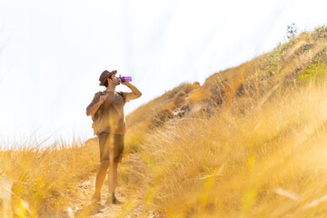 Caucasian man backpacker drinking water from a bottle during hiking on mountain hill in sunny day....