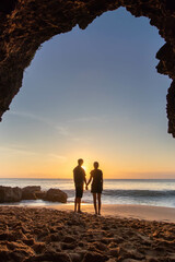 Photo of a couple at Tegal Wangi Beach, Jimbaran, Bali taken from inside the cave while sunset. People are outside the cave on the beach at afternoon.