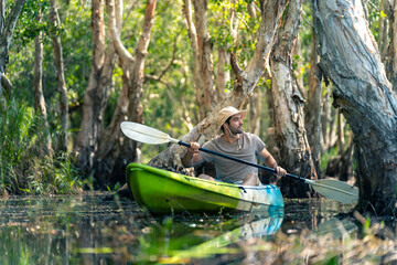 Caucasian man tourist enjoy outdoor lifestyle kayaking at mangrove forest on summer vacation. Handsome guy traveler canoeing or row the boat on lake. Environmental ecotourism and solo travel concept.