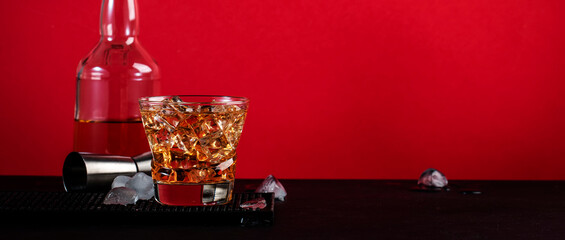 Godfather cocktail with scotch whiskey, almond amaretto liqueur and ice cubes.. Black and red background, steel bar tools, banner - obrazy, fototapety, plakaty
