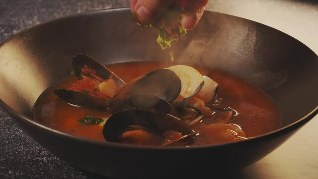 Tasty fish soup boiling. Spreading parsley on  Mediterranean fish soup with mussels, clams, prawns, tomato. Tasty hot soup