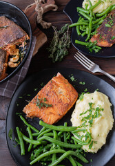 Pan fried salmon with skin. Served with mashed potatoes and green beans on a dark plate on rustic and wooden table background. Top view