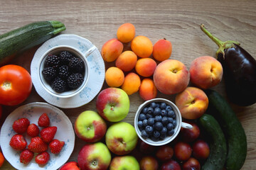 Berries in vintage porcelain dishes, other healthy fruit and vegetable on wooden table. Top view.