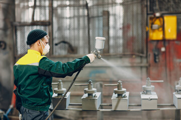 Powder primer coating of metal parts. Worker man in a protective suit sprays powder paint from gun