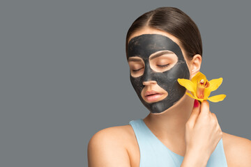 Cosmetologist doing carbon peeling procedure to beautiful girl with yellow orchid in a beauty salon. Hardware cosmetology treatment.