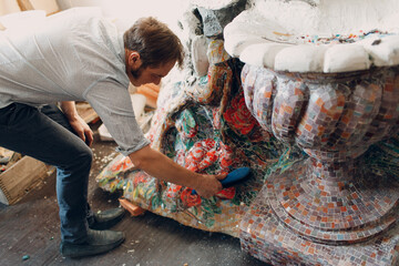 Man mosaics master in hat making smalt glass mosaic panel. Male mosaicist at work