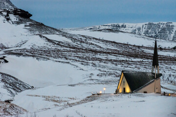 imagen de una iglesia de Islandia iluminada con las montañas nevadas de fondo 
