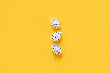 white Easter eggs with stripes and a dot with confetti on a bright yellow background. layout for easter.