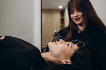 Young woman undergoing procedure of eyebrow permanent makeup in beauty salon
