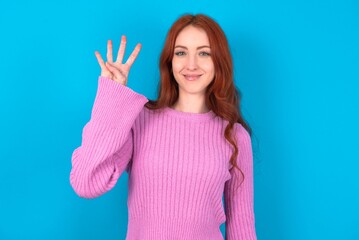 young woman wearing pink sweater over blue background showing and pointing up with fingers number four while smiling confident and happy.