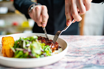 man hands with fork and knife eating beef steak and salad in cafe