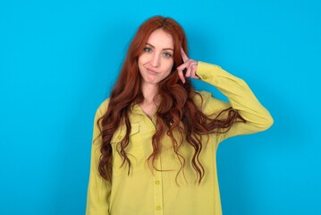 young woman wearing green sweater over blue background tries to memorize something, keeps fore...