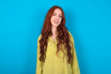 Fototapeta premium young woman wearing green sweater over blue background winking looking at the camera with sexy expression, cheerful and happy face.