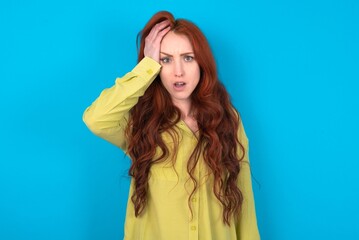 Embarrassed young woman wearing green sweater over blue background with shocked expression, expresses great amazement, Puzzled model poses indoor