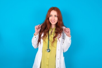 young doctor woman wearing medical uniform over blue background clenches fists and awaits for...