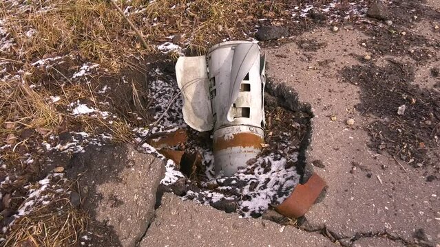 The metal tail of a rocket artillery shell sticks out of the broken asphalt on the street of a Ukrainian city. The Russian army is shelling peaceful cities. Real War 2022-2023
