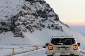 imagen de un coche por una carretera nevada con una montaña nevada de fondo y el cielo amaneciendo 