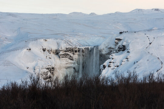imagen de una cascada entre las montañas nevadas y los árboles secos 