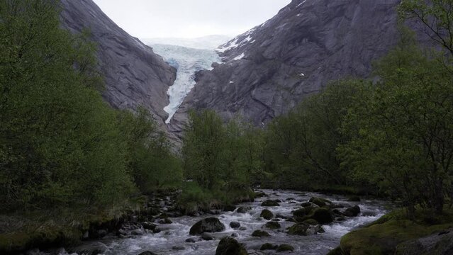 Briksdal glacier with glacial river in the foreground on a rainy day in Norway
