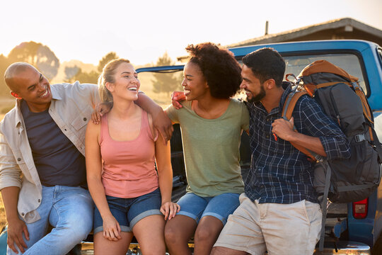 Group Of Friends Sitting On Tailgate Of Pick Up Truck On Road Trip To Cabin In Countryside