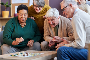 Group of senior people playing board games together at retirement home with emotional faces