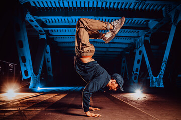Young cool man break dancer posing on urban bridge at night