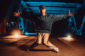 Young cool man break dancer posing on urban bridge at night