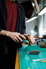 A man's hand holds pieces of leather for a leather wallet in his workshop. The process of working with natural brown leather. The craftsman holds the craft
