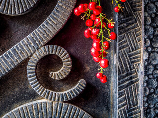 Black, rough forged iron surface with curved shaped decor and a bunch of bright red peppercorn...