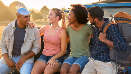 Group Of Friends Sitting On Tailgate Of Pick Up Truck On Road Trip To Cabin In Countryside