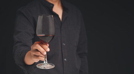 Close-up of hand holding a red wine glass while standing on a black background