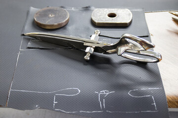 A photo of professional tailor's scissors on a piece of perforated leather, highlighting the precision and skill involved in the art of tailoring.