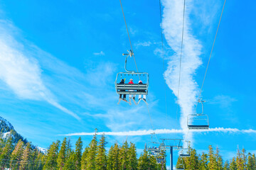 Ski Lift Carrying Skiers Over Pine Trees Against Blue Sky